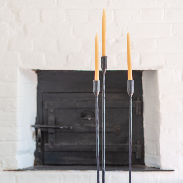 Join I Three tapered candles in candle holders in front of a period house bakery oven 
